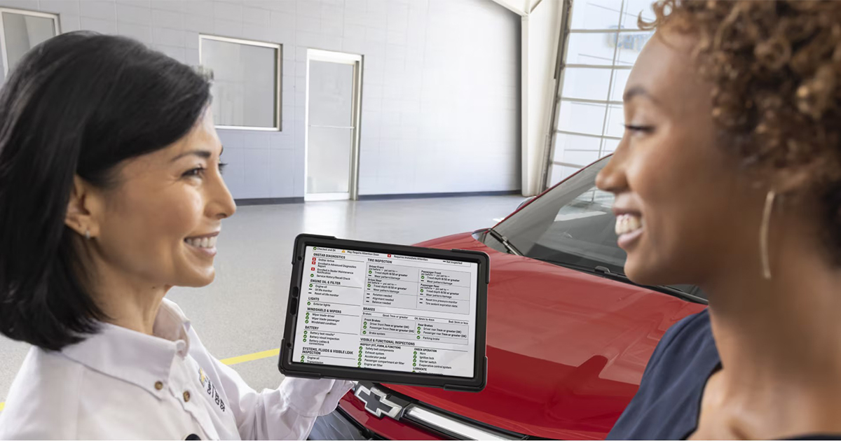 Chevrolet service representative showing multi-point inspection checklist on tablet to customer with red vehicle in background