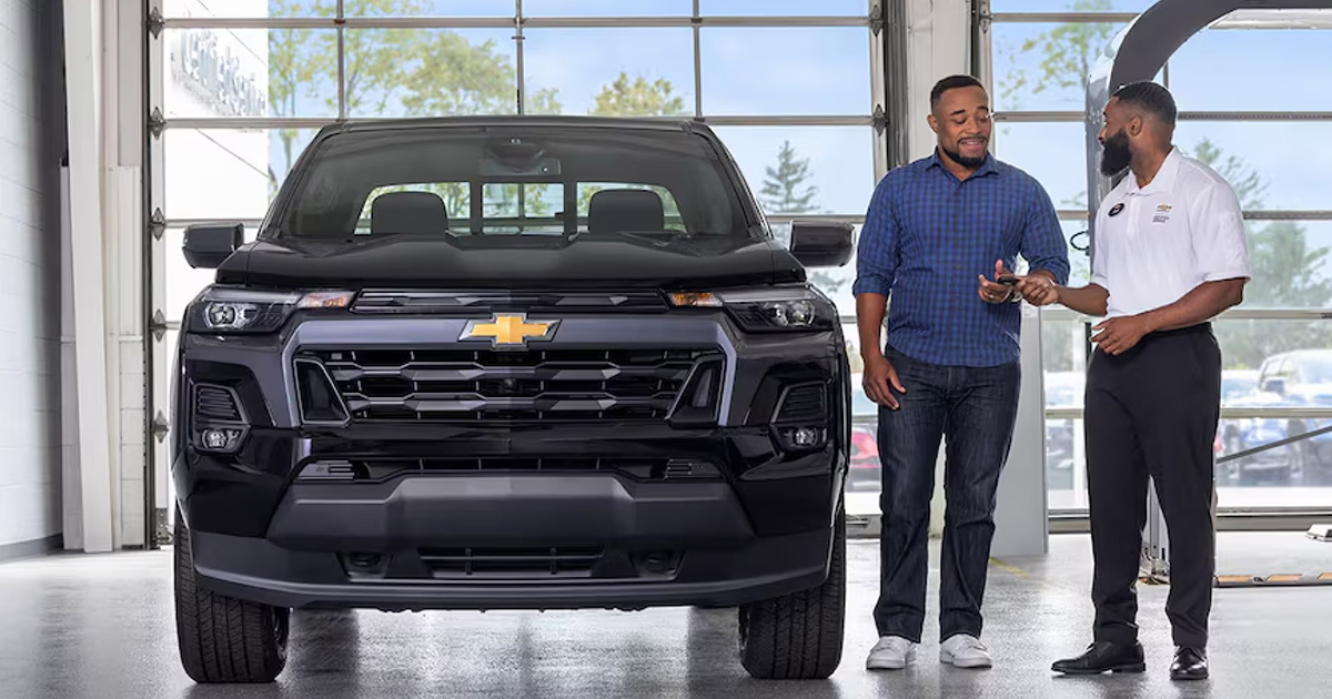 Customer and Chevrolet service advisor discussing black Chevrolet Colorado in dealership service bay
