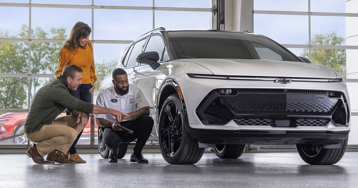 Chevrolet service technician discussing tire options with customers next to white Chevrolet RS model in dealership
