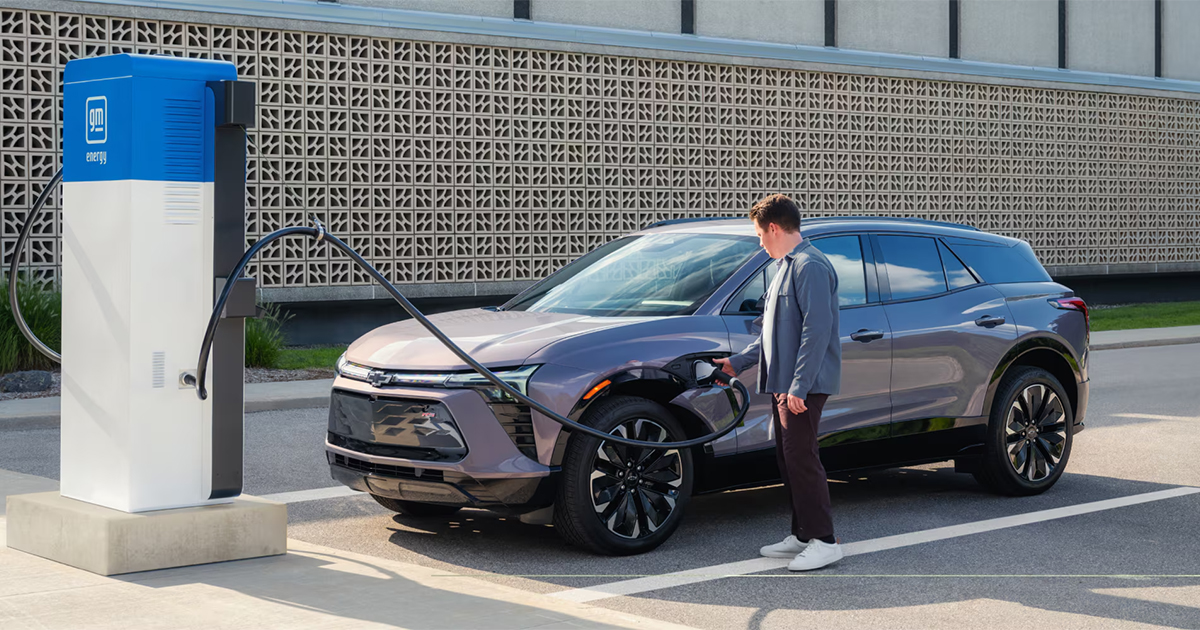 Man using public DC fast charging station to charge silver Chevrolet Blazer EV in urban setting