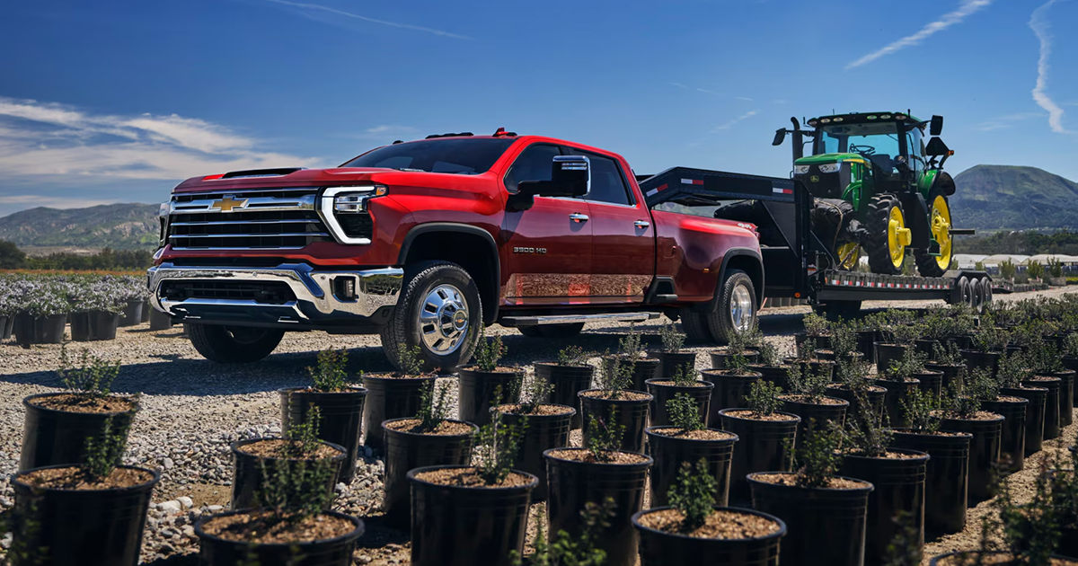 Red Chevrolet Silverado HD pickup truck towing large agricultural trailer with green tractor