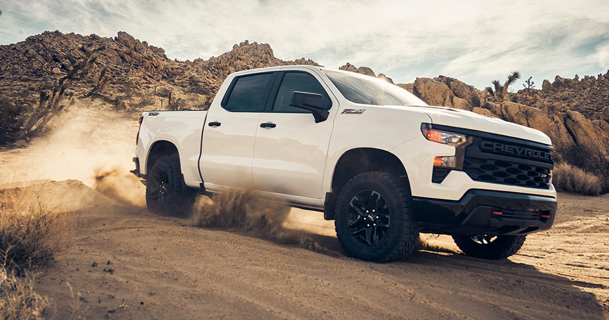 White 2025 Chevrolet Silverado 1500 ZR2 Bison kicking up sand in desert terrain with rock formations