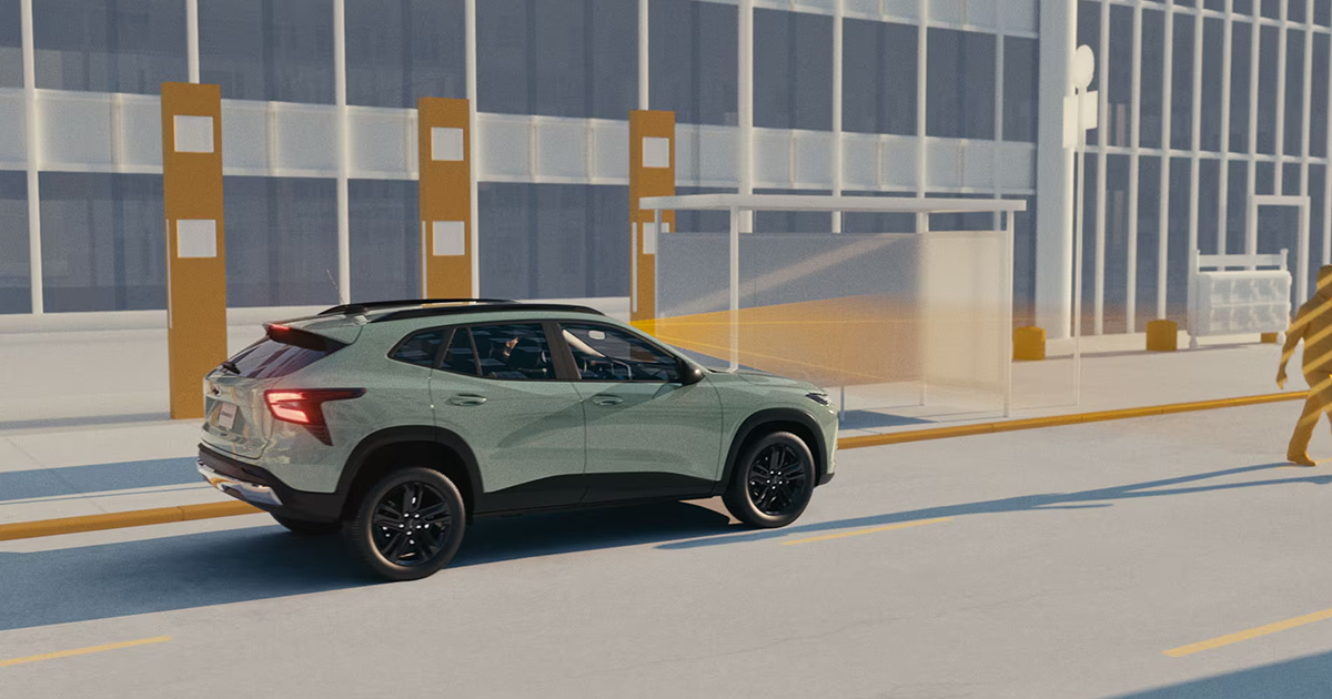Sage green Chevrolet Trax SUV on city street demonstrating pedestrian detection safety system with person walking in front of vehicle