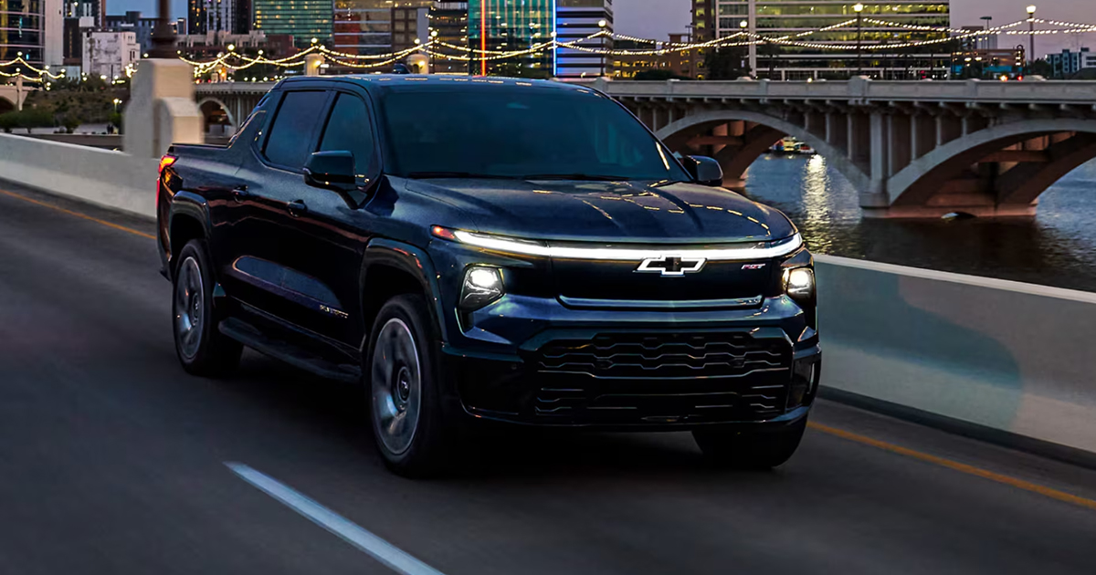 Dark blue Chevrolet Silverado EV pickup truck driving on illuminated city bridge at night