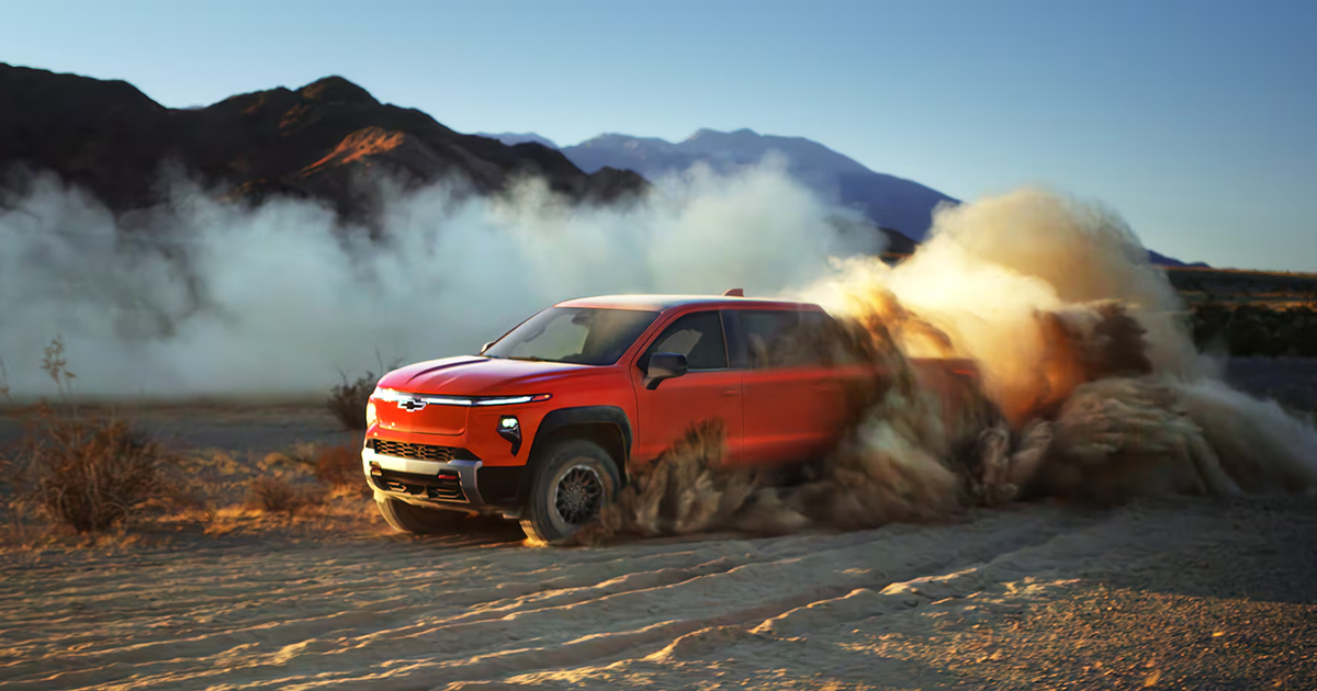 Red Chevrolet Silverado EV Trail Boss kicking up dust while off-roading in desert with mountain backdrop