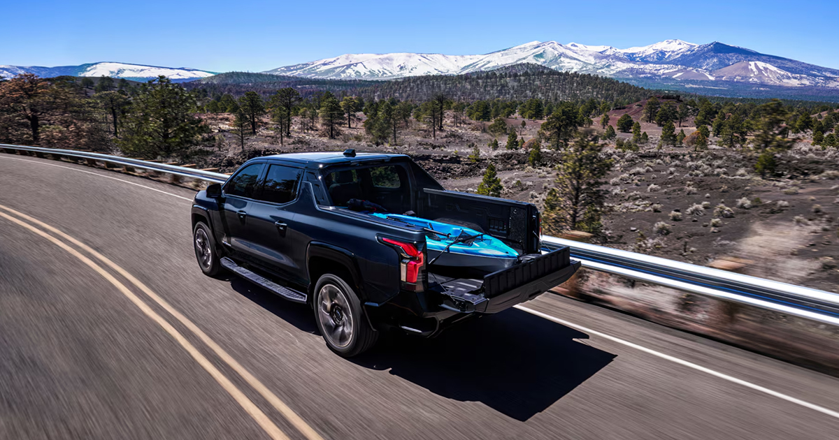 Black Chevrolet Silverado EV with blue cargo in truck bed driving on mountain highway