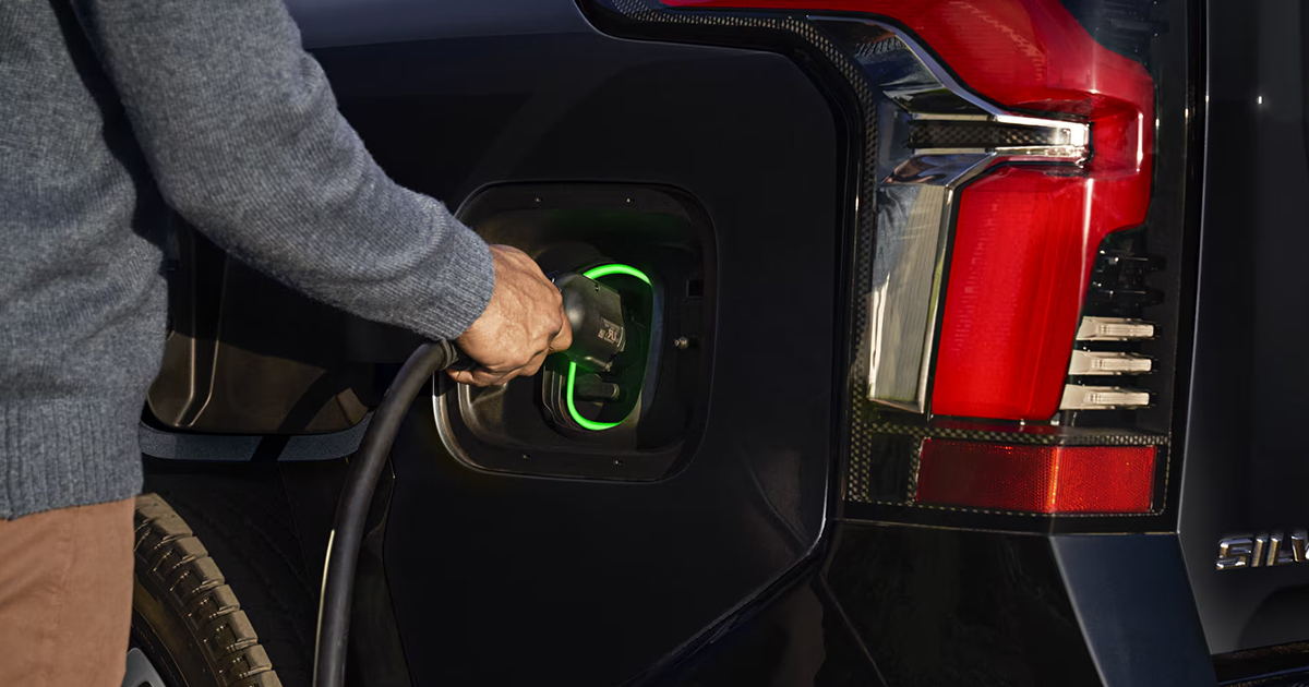 Close-up of person connecting charging cable to Chevrolet Silverado EV charging port with green LED indicator