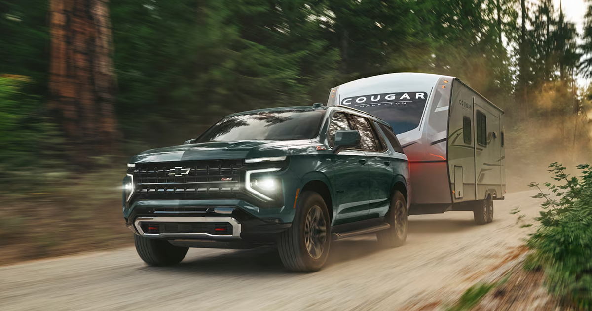 Dark green 2025 Chevrolet Tahoe Z71 towing Cougar travel trailer on dirt road with motion blur demonstrating towing capability