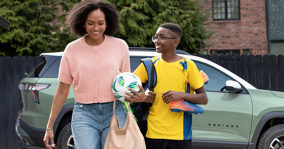 Mother and son with soccer gear walking beside light green Chevrolet Equinox in residential neighborhood