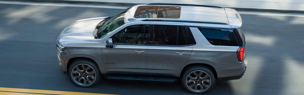 A silver SUV with a roof cargo box drives along a city street.