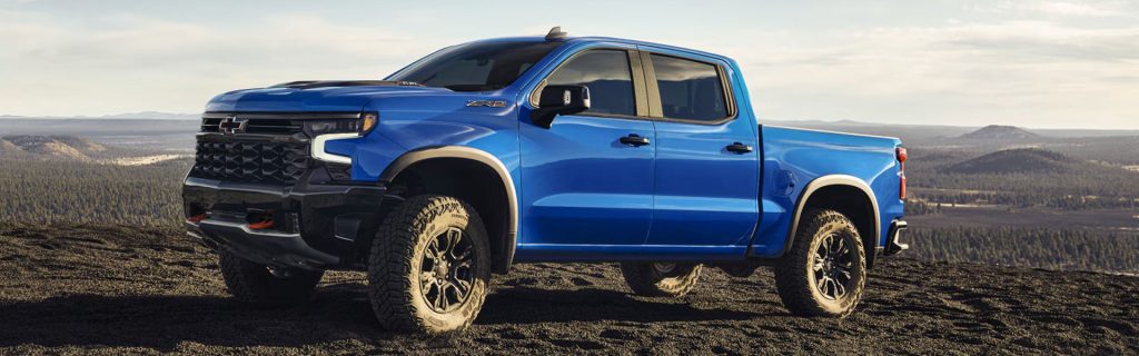 Blue off-road pickup truck parked on a rugged hilltop overlooking a wide forested landscape.