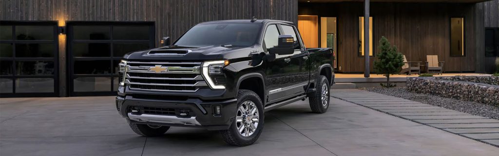 Black Chevrolet pickup truck parked in front of a modern wood-paneled house with a driveway at dusk.