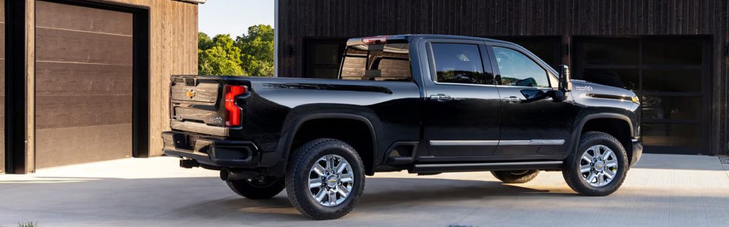 Black Chevrolet Silverado HD pickup truck parked outside a modern building, showcasing its rugged design and spacious crew cab.
