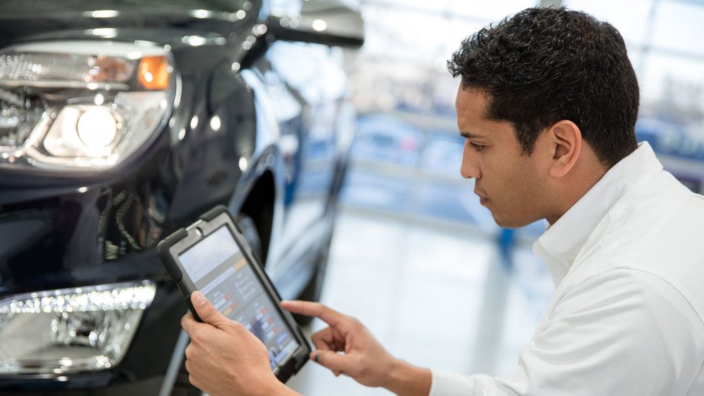 Service technician using a diagnostic tablet to inspect a vehicle in a professional automotive service center.