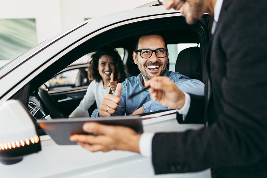 A man and woman sitting inside car showing thumbs up.